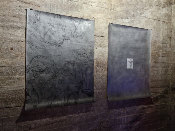 Twee grote tekeningen op papier tegen een betonnen wand